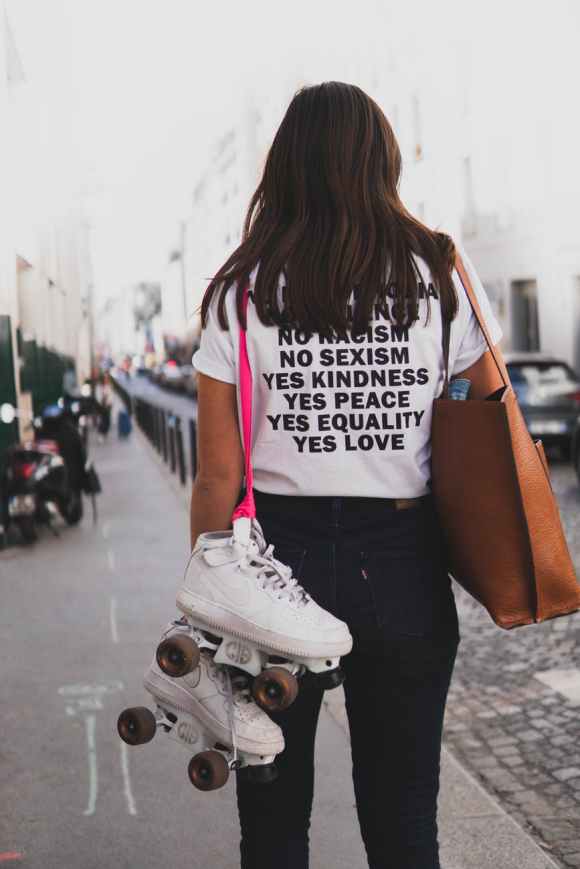 woman in white shirt and denim jeans carries skate shoes and tote bag